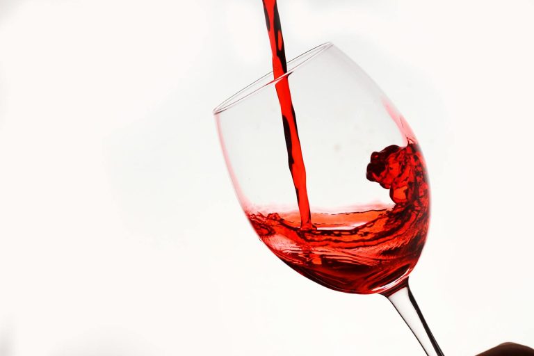 Elegant shot of red wine being poured into a tilting glass against a white background.